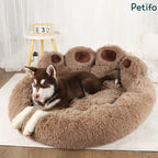 A brown and white husky puppy resting inside a large, fluffy brown paw-shaped dog bed.