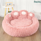 An empty pink fluffy paw-shaped dog bed displayed in a bright room with a small side table.
