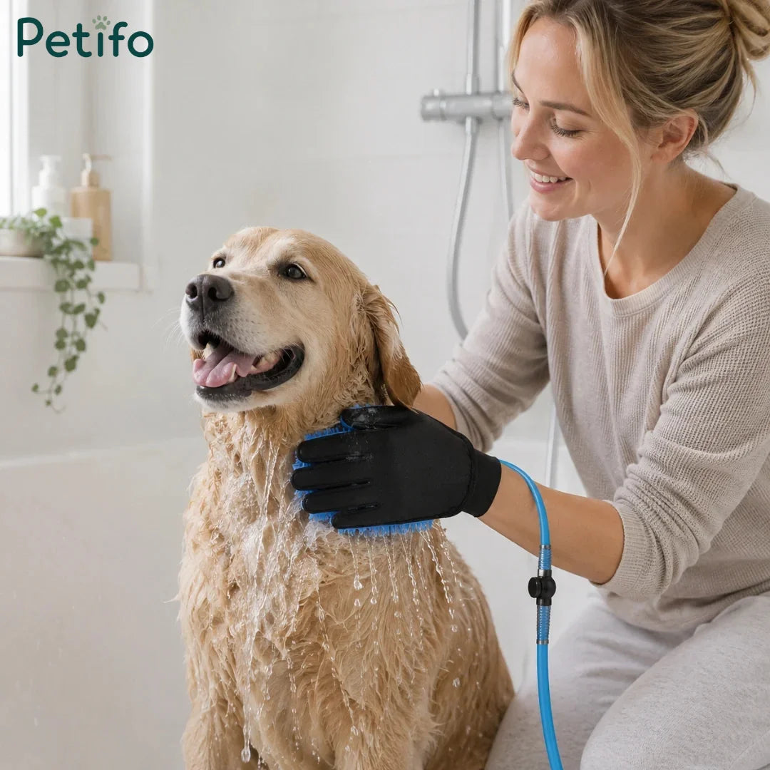 Woman happily bathing a golden retriever with a blue grooming glove in a bathtub.