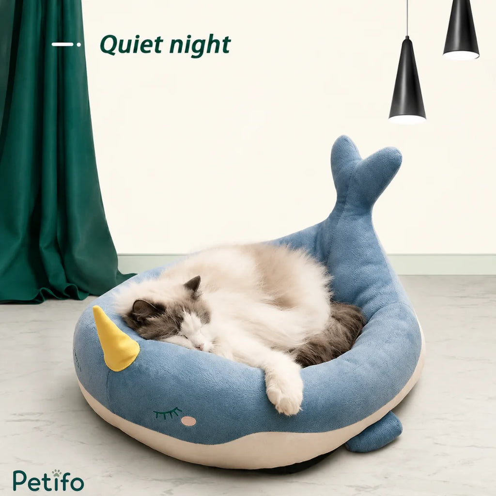 Fluffy cat sleeping peacefully inside a blue narwhal-themed Petifo plush cat bed.