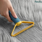A hand using a blue and yellow pet lint remover on a fluffy gray rug.