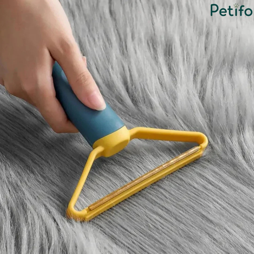 A hand using a blue and yellow pet lint remover on a fluffy gray rug.
