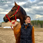 Woman standing outdoors holding a brown horse wearing a bright red halter.