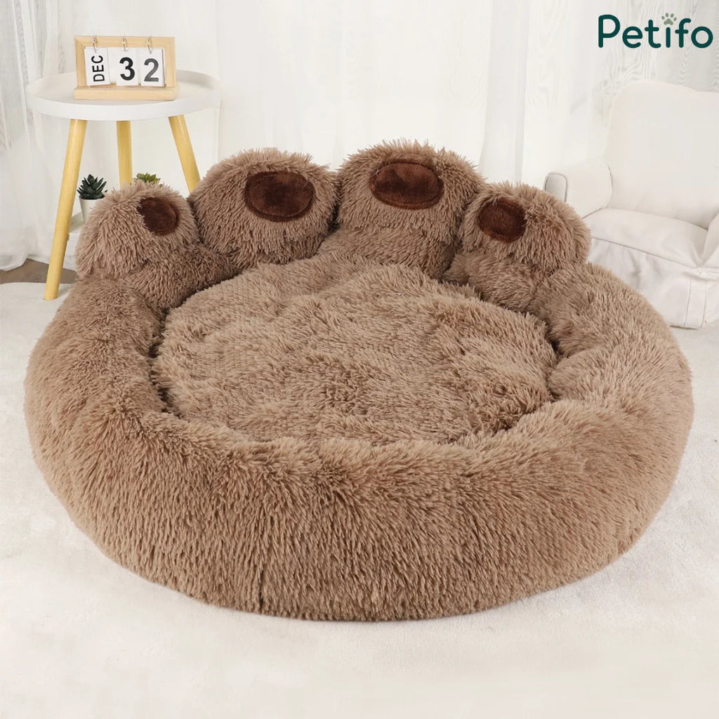 Brown plush paw-shaped dog bed with a calendar and mini table in the background.