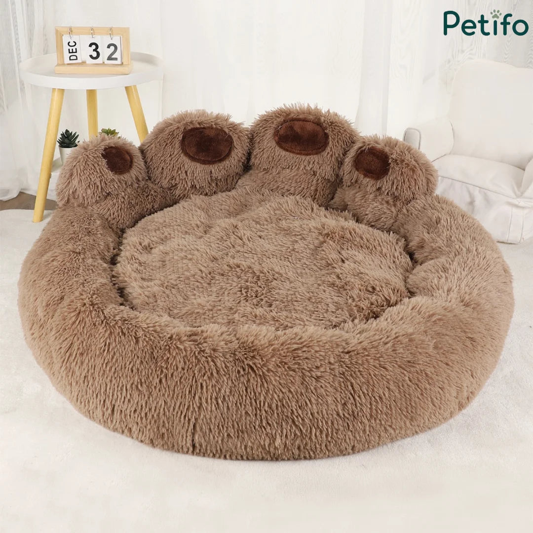Brown plush paw-shaped dog bed with a calendar and mini table in the background.