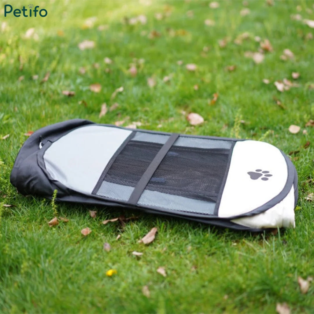Compact folded Petifo portable dog playpen lying flat on a green grass lawn.
