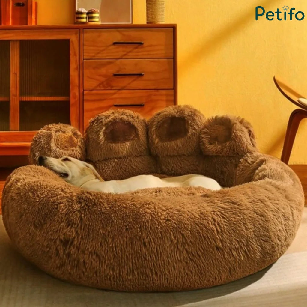 A cute dog sleeping peacefully inside a cozy brown plush paw bed set against a warm yellow room.