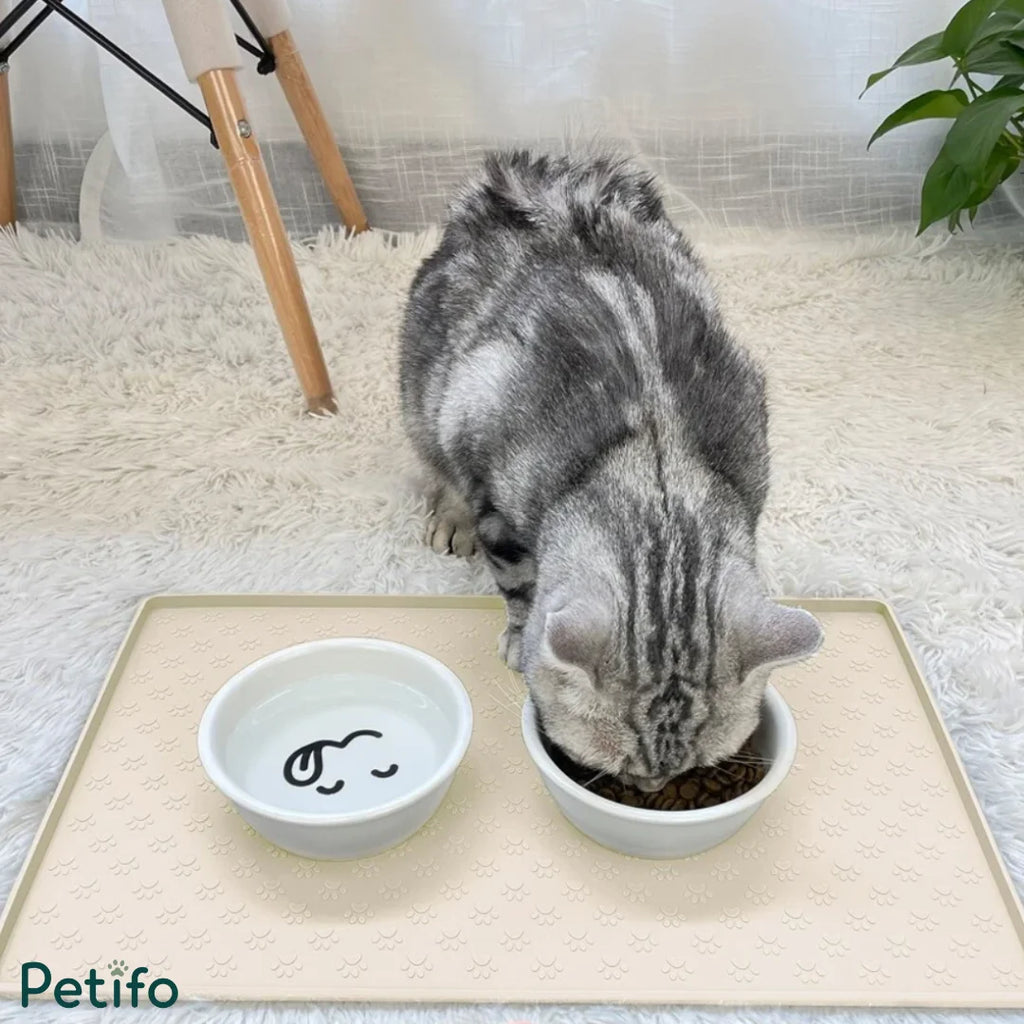 A gray tabby cat eating from a bowl placed on the beige pet silicone dining mat.
