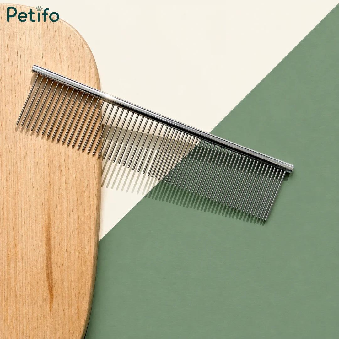 Flatlay product shot of the Petifo metal pet grooming comb resting against a wooden board and a green and cream background.