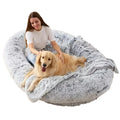 Woman sitting and petting a happy golden retriever in a fluffy grey human dog bed.