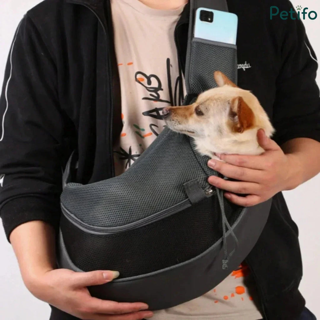 Person carrying a small dog securely inside a grey mesh hands-free pet sling.
