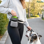 A handler pulling a toy from a hands-free dog treat pouch while walking an australian shepherd outdoors.