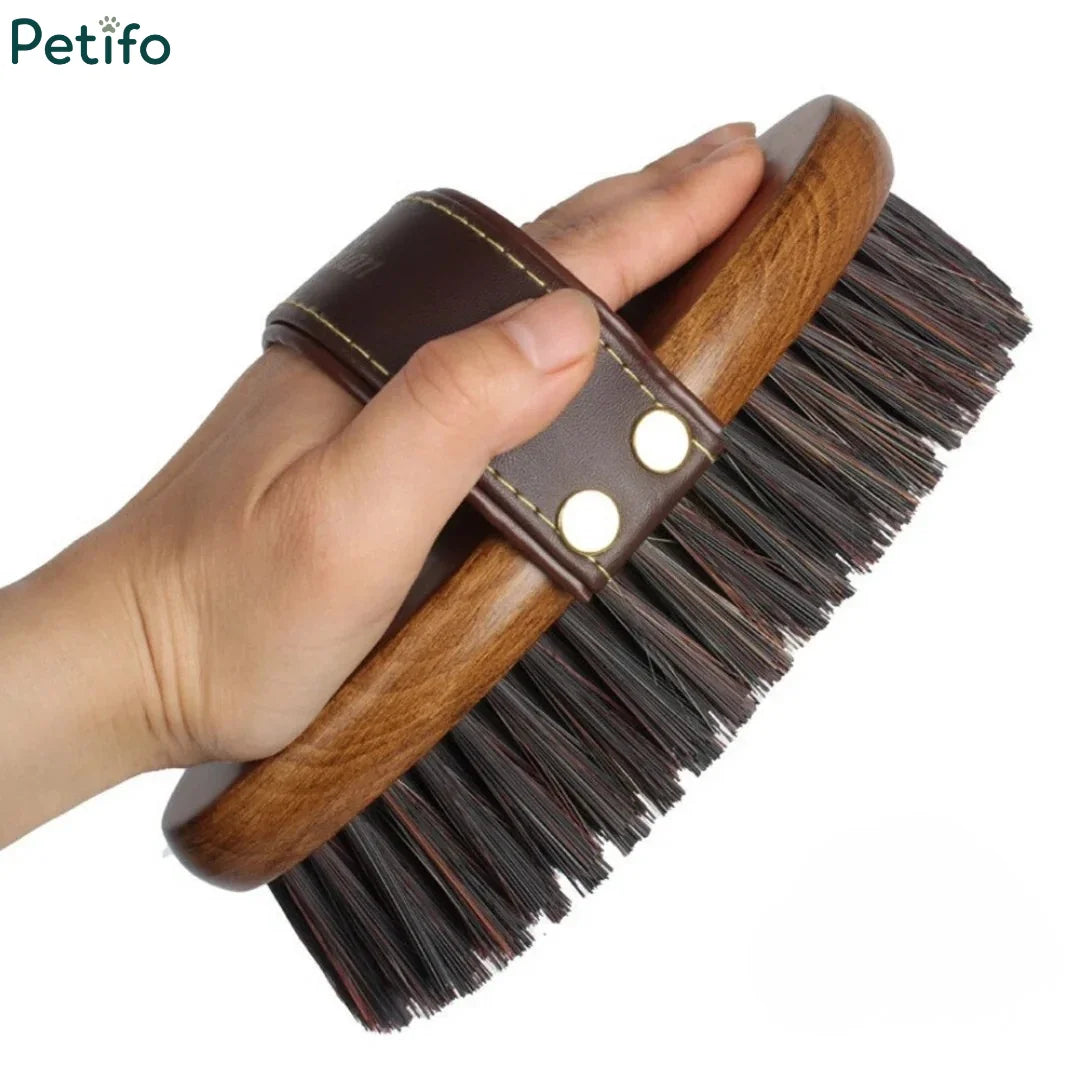 Person holding an ergonomic wooden horse grooming brush by its leather hand strap.