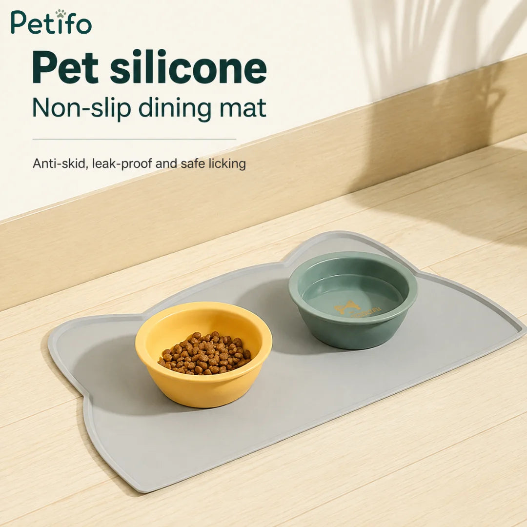 Gray pet silicone non-slip dining mat displayed with a yellow food bowl and a green water bowl on a wooden floor.