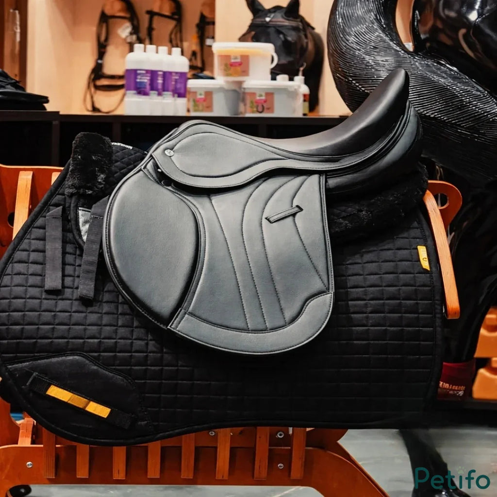  Black English saddle resting on a black quilted saddle pad on a wooden rack.