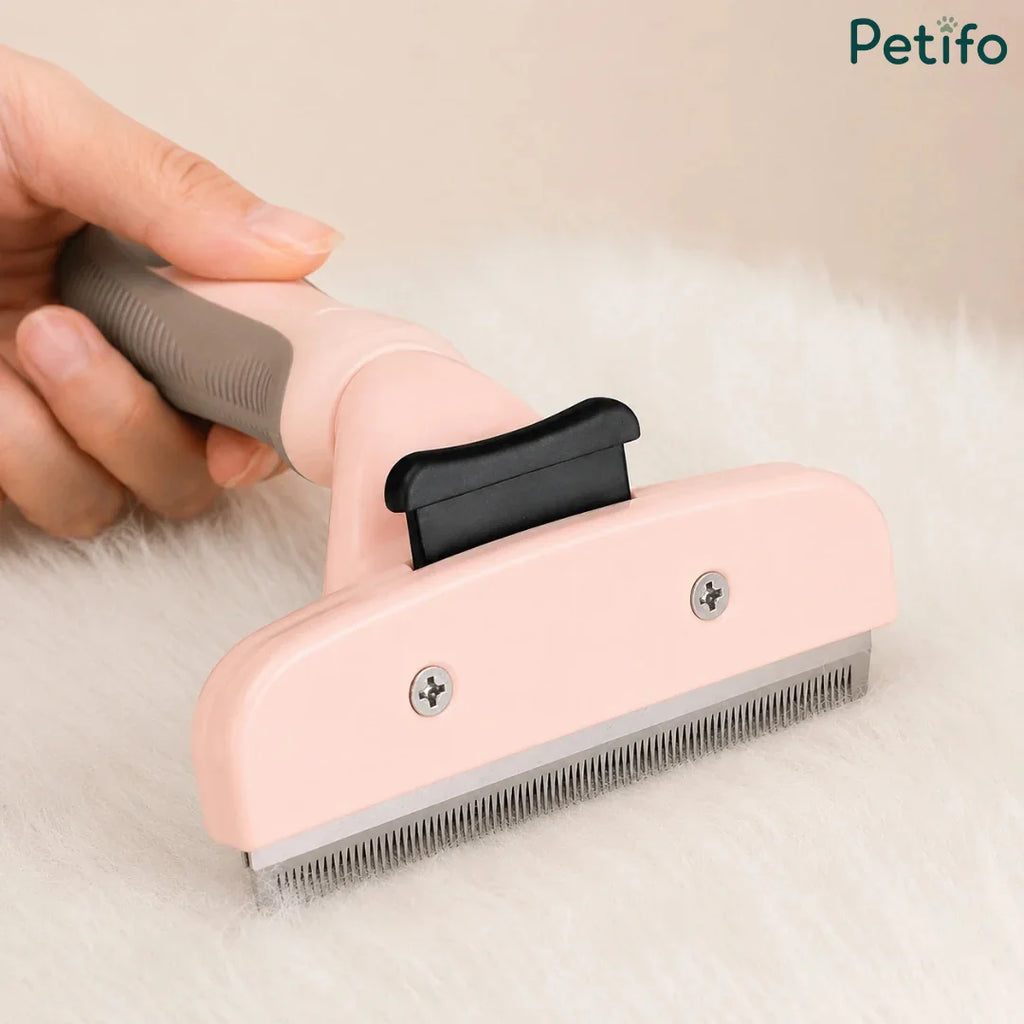 Hand holding a pink pet grooming brush against a soft white fur background.