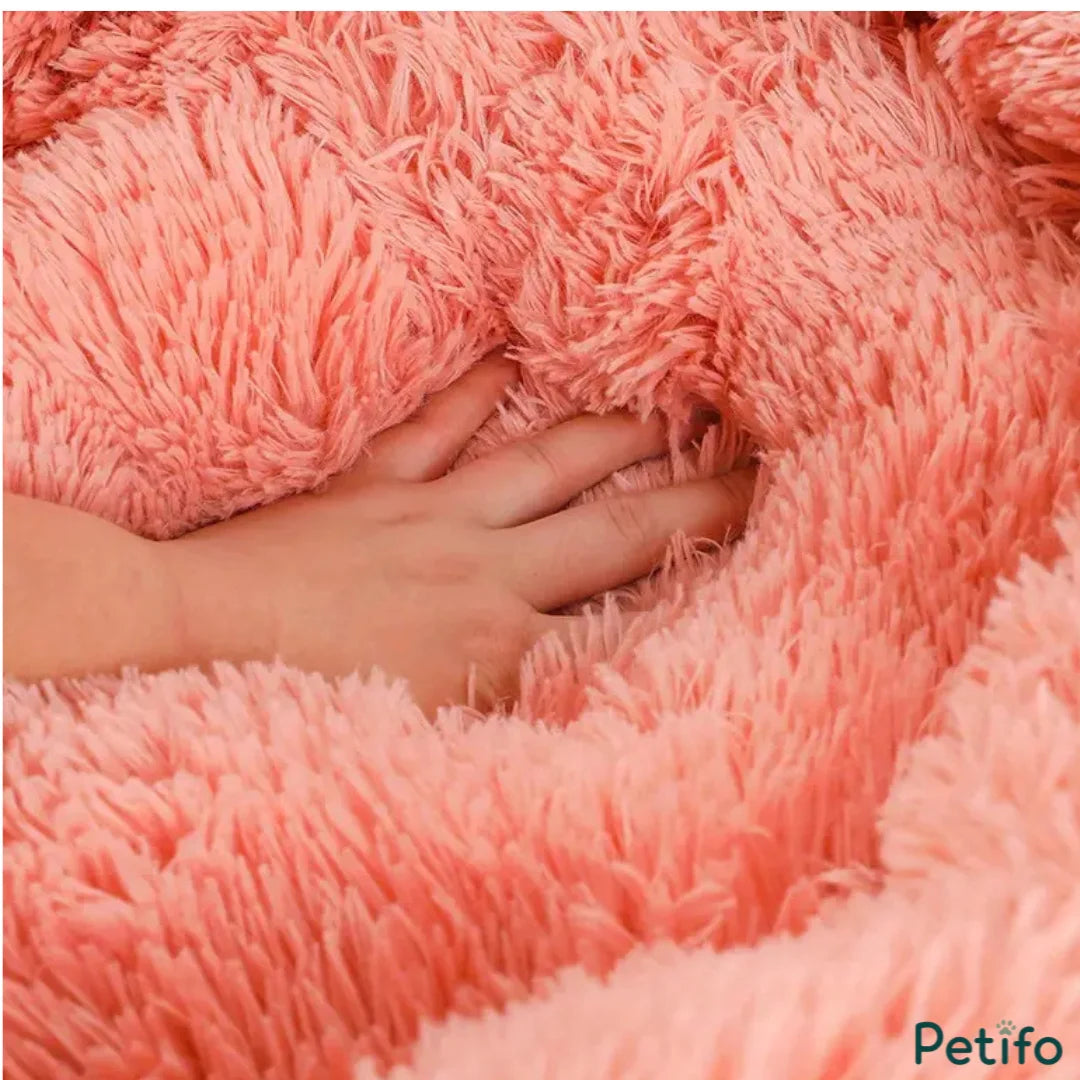 Close-up of a hand pressing into a soft, textured pink plush pet bed.