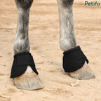Horse wearing black protective hoof boots on sandy ground