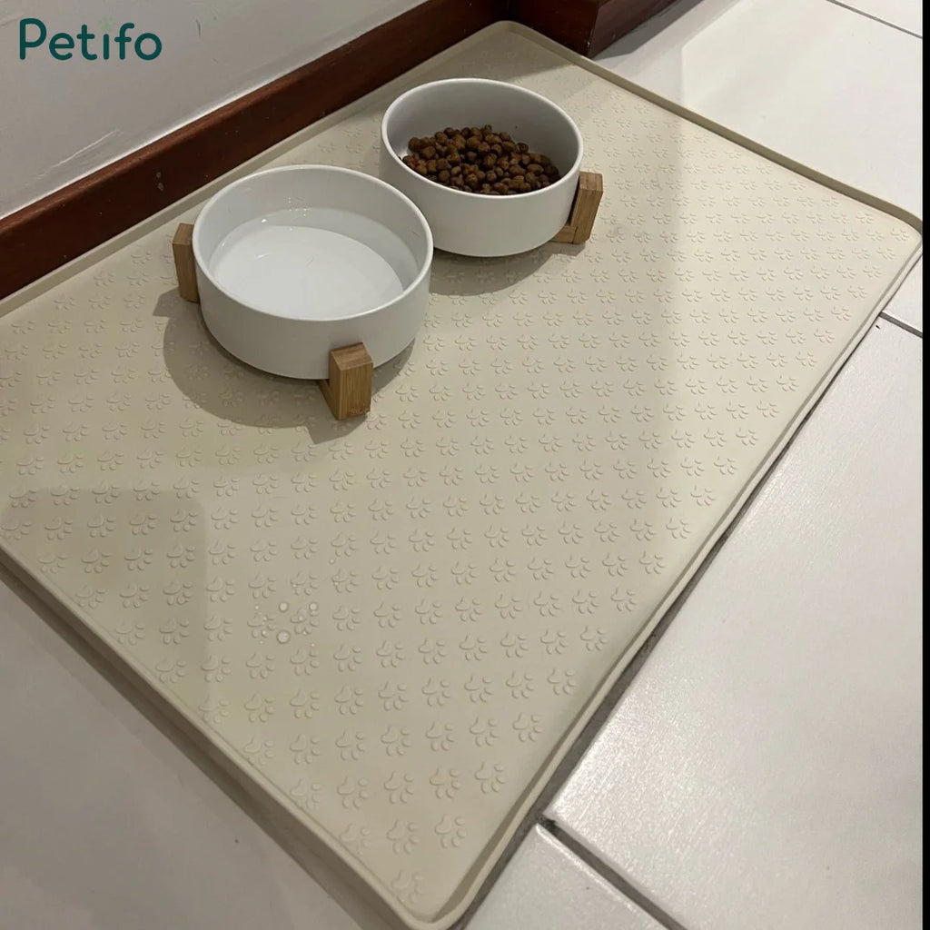 Beige pet silicone mat holding two white bowls with wooden stands containing food and water on a tiled floor.