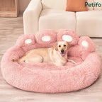 A golden retriever lying relaxed in a soft pink paw-shaped plush dog bed near a white couch.