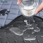 Water being poured onto a black waterproof pet training mat to demonstrate liquid resistance and absorption.