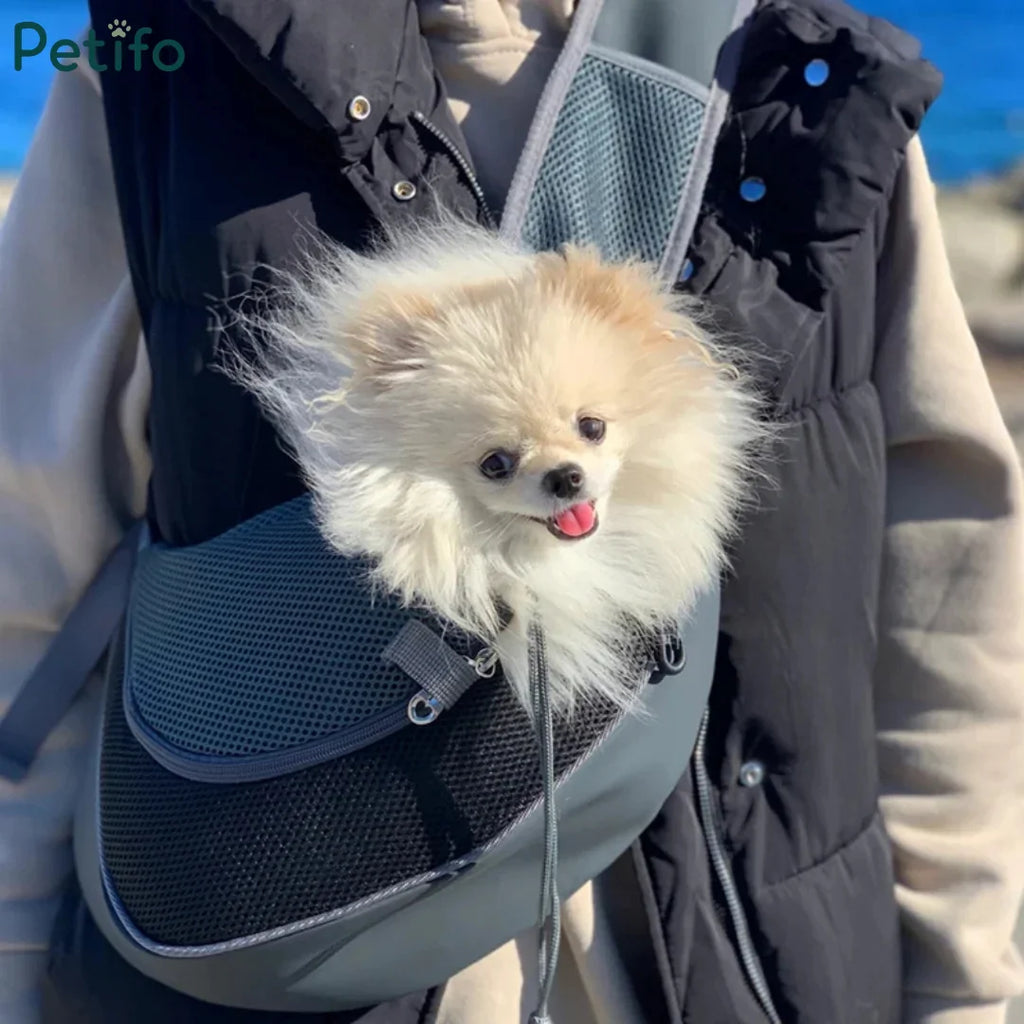 Fluffy white Pomeranian puppy riding comfortably inside a grey mesh pet sling bag.