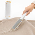 Hand holding a white and gold lint remover brush next to its matching self-cleaning base while removing lint from a beige sweater.