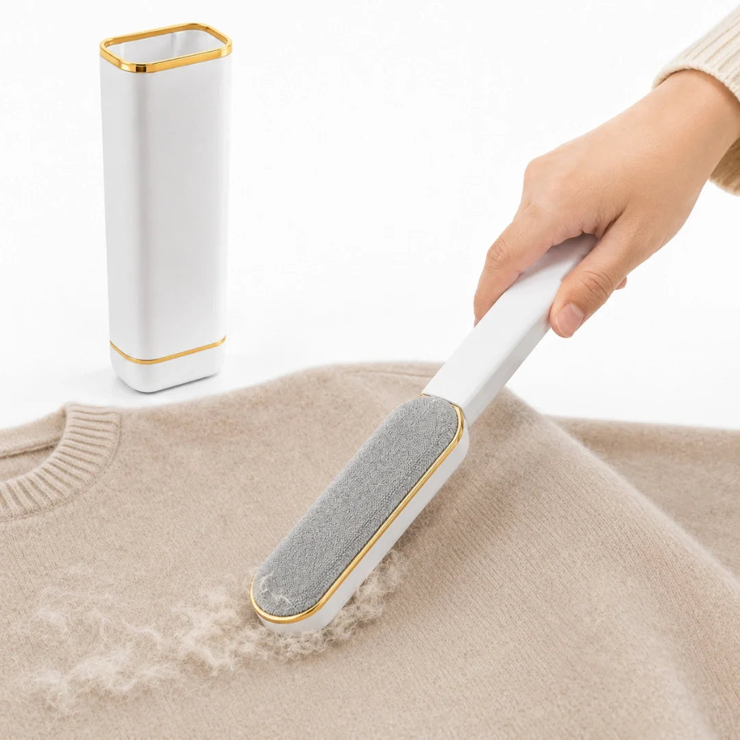 Hand holding a white and gold lint remover brush next to its matching self-cleaning base while removing lint from a beige sweater.